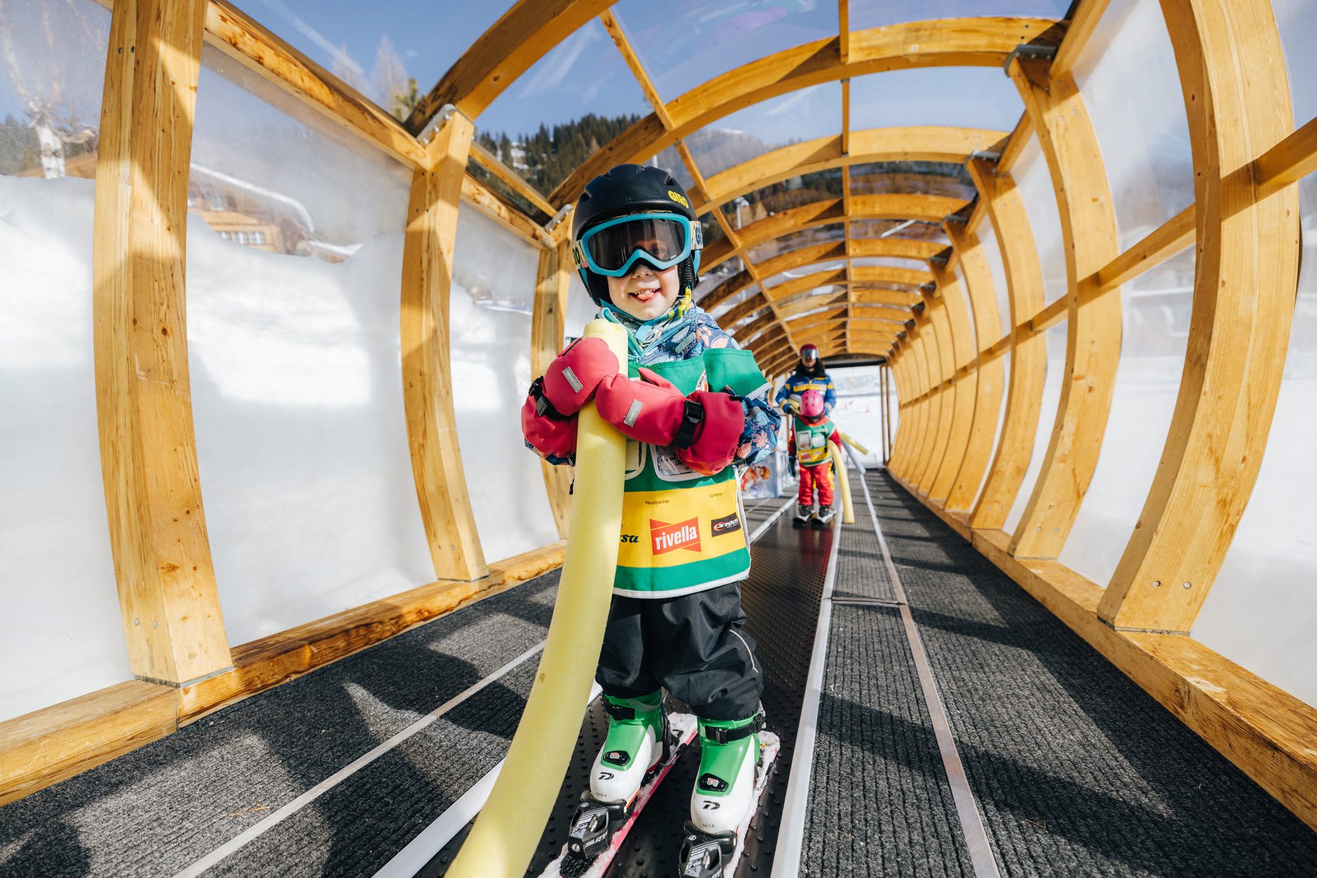 Kind fährt auf dem gedeckten Zauberteppich im Kinderland der Skischule Arosa nach oben