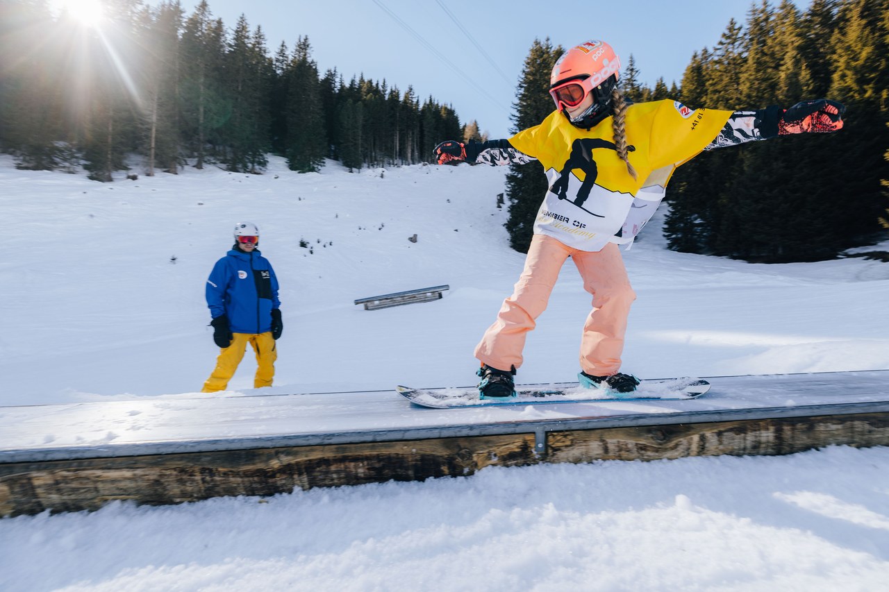 Kind der Skischule Arosa fährt im Red-Prince-Level mit dem Snowboard über eine Box im Snowpark